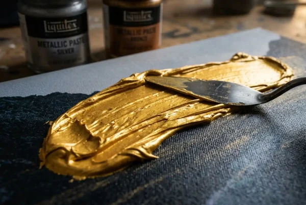 Ein Edelstahl-Malmesser zieht eine dicke, leuchtende Linie aus 3D-Goldpaste über einen auf Keilrahmen gespannten Kunstdruck.